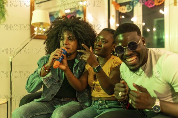 Multi-ethnic friends singing karaoke sitting on the sofa during night party at home