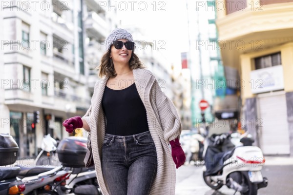 Lifestyle, young Caucasian blonde girl enjoying and smiling in the city in winter. Strolling with sunglasses and red gloves