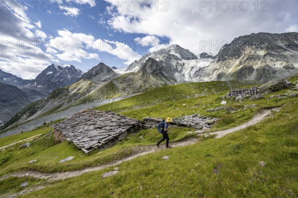 Mountaineers on a hiking trail, Alpine huts covered with slate slabs, mountain landscape near Arolla, behind mountain peak Mont Collon and glacier Glacier de Tsijore Nouve, Valais, Western Alps Switzerland