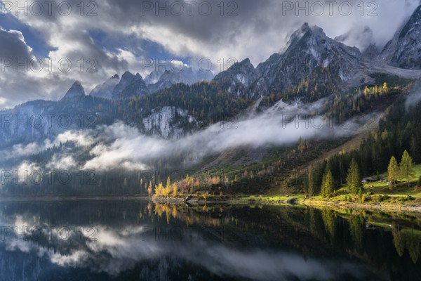 The Vordere Gosausee in autumn with a view of the Gosaukamm. Cloudy sky with sun. Trees in autumn leaves. Reflection. Overcast with clouds. Vorderer Gosausee, Gosau, Gosau valley, Salzkammergut, Upper Austria, Austria, Europe
