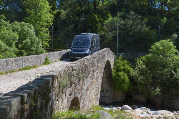 A van drives over a historic stone bridge, surrounded by lush vegetation and sunny weather, motorhome on bridge, Puente Parral, Roman bridge Parral, Garganta Jaranda, Jaranda gorge, Jarandilla de la Vera, Cáceres, Caceres, Extremadura, Spain, Europe