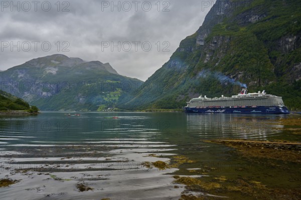 A large cruise ship, Mein Schiff 6, lies in the fjord, surrounded by green mountains under a cloudy sky, Geiranger, Geiranger Fjord, Stranda, Romsdal, Norway, Europe