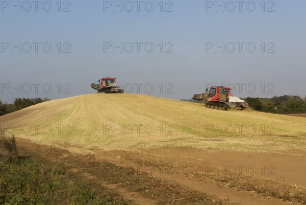 Piston Bully tracked bulldozer vehicles building silage clamp of sweetcorn maize in field stored for biofuel, Alderton, Suffolk, England, UK