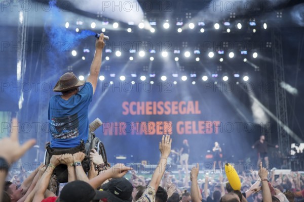 A wheelchair user with pyro in his hand is carried over the audience during the performance of the band Feine Sahne Fischfilet at the Highfield Festival on Saturday, Störmthaler See, 17/08/2024
