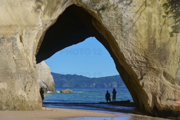 Silhouettes of people under a large rock arch on the beach overlooking the sea, Cathedral Cove, Hahei, Coromandel Peninsula, North Island, New Zealand, Oceania