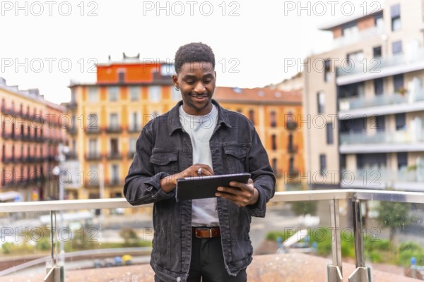 Frontal three quarter length photo of a happy young african man using digital tablet standing in a city