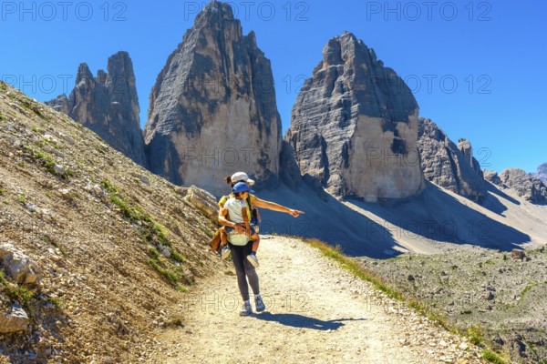 Woman carrying child hiking and pointing at the landscape near tre cime di lavaredo, dolomites, a famous landmark of the italian alps