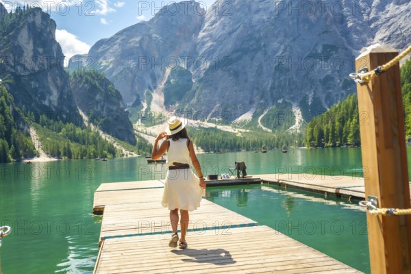 Tourist walking on a wooden pier, enjoying the scenic view of lake braies and the surrounding dolomites mountains in summer