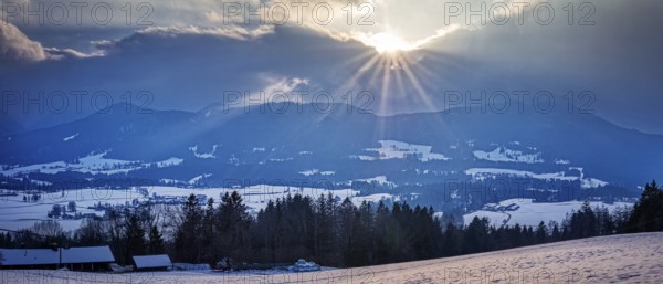 Winter landscape with mountains in the background and sunbeams through the clouds, Fischbachau