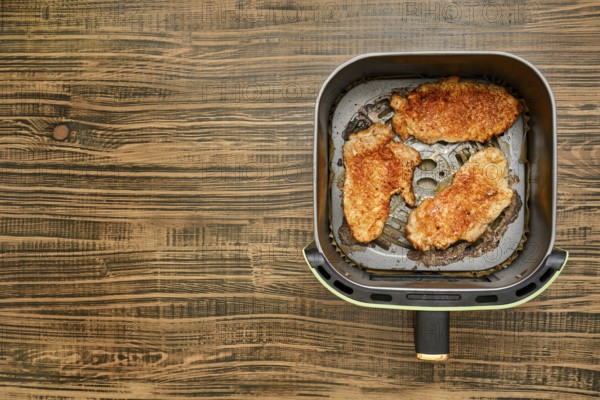 Three pork chops are sizzling in an air fryer basket, each one showcasing a crispy golden crust