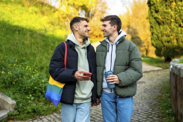 Happy caucasian gay couple holding hands and walking in a park, enjoying a relaxing moment together