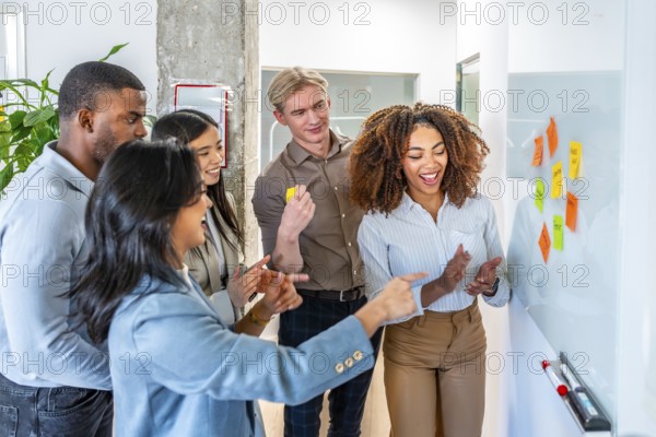 Diverse colleagues brainstorming and planning using colorful sticky notes on a whiteboard, showcasing teamwork and collaboration in a modern office environment