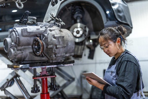 Young asian female mechanic using digital tablet while inspecting gearbox in a car workshop