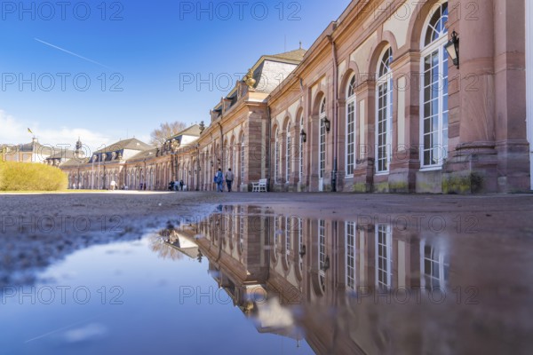 Large building with elaborate architecture reflected in a puddle under a blue sky, Schwetzingen Palace Gardens, Germany, Europe