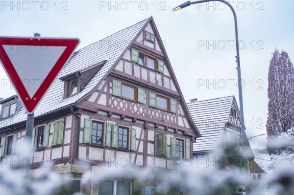 Snow-covered half-timbered house with green shutters in front of a clear sky and a traffic sign, Aidlingen, Böblingen district, Germany, Europe