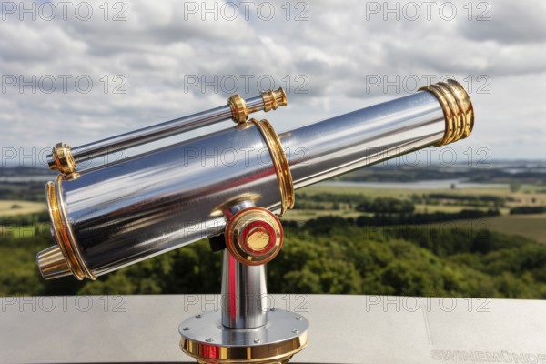 Metallic telescope points into the distance over a vast landscape under a cloudy sky, Rügen, Granitz Castle