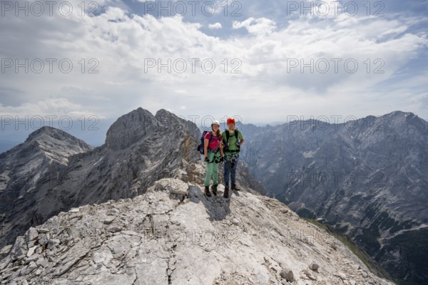Couple, two mountaineers with helmets on a narrow rocky ridge, crossing the Jubiläumsgrat, view of rocky mountain peaks and Alpspitze, Wetterstein range, Bavaria, Germany, Europe