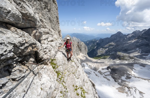 Mountaineer with helmet in a secured via ferrata, Zugspitz via ferrata, ascent to the Zugspitze, view of mountain basin with snowfield of the Höllentalferner and Höllental, Wetterstein range, Bavaria, Germany, Europe