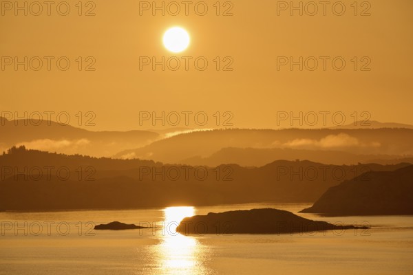 A soft orange sunrise behind the dark silhouettes of mountains and a calm sea, sunbeams reflecting in the North Sea, autumn, Bergen, North Sea, Norway, Europe