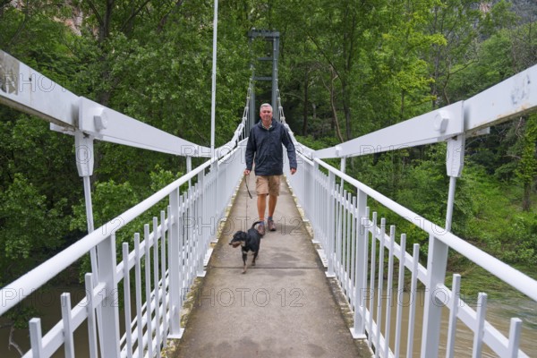 Man with dog on a suspension bridge, surrounded by green nature, during a relaxing walk, Pineios River, Tempe Valley, Tembi Valley, Thessaly, Greece, Europe