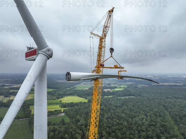 Dorsten, North Rhine-Westphalia, Germany, construction of a wind turbine. A large mobile crane lifts a rotor blade to the nacelle on the tower. Here, the blade is mounted directly on the motor hub. Große Heide wind farm, Europe