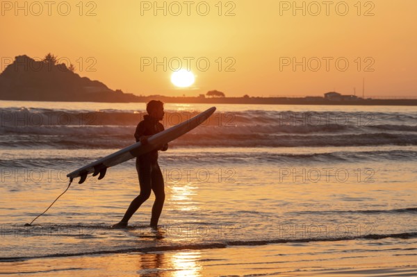 Crescent City, California - A surfer takes his board out of the water as the sun sets over the Pacific Ocean in northern California