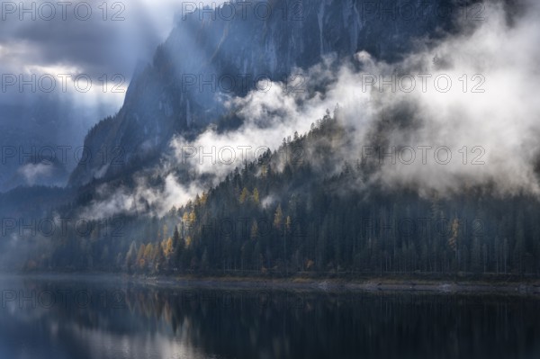 The Vordere Gosausee in autumn with a view of the Gosaukamm. Rays of sunshine shine through the clouds. Forest shrouded in clouds. Vorderer Gosausee, Gosau, Gosau valley, Salzkammergut, Upper Austria, Austria, Europe