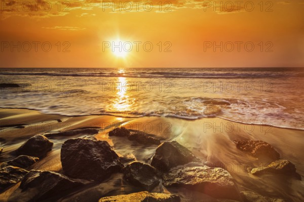 Tropical beach vacation background, waves and rocks on beach on sunset with beautiful cloudscape. With lens flare and light leak