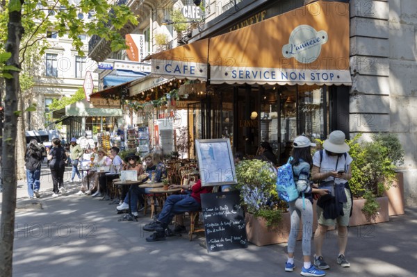 Street café with several guests outside under an orange awning on a sunny day, Paris