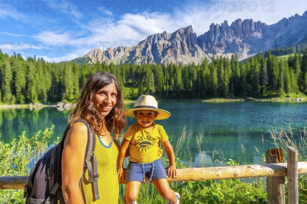 Mother and son enjoying the stunning scenery of lake carezza with the latemar mountain range in the background, dolomites, italy