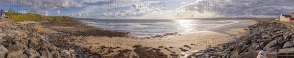 Extensive beach with rocks and coastline under a cloudy sky, interspersed with sunlight, Lahinch Beach