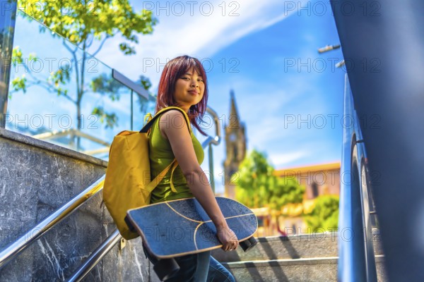 Cool asian young female skater turning to smile at camera walking up stairs in the city