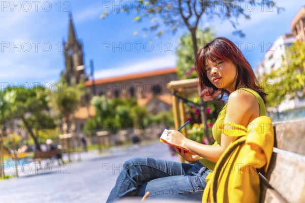 Asian cool young woman sketching sitting on a bench in the city in a sunny day