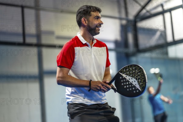 Mature athletic man playing paddle tennis with friends in an indoor court