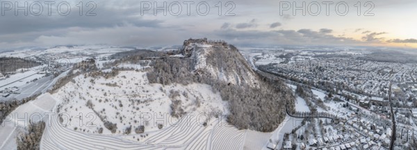 Aerial view, panorama of the snow-covered Hegau volcano Hohentwiel with Germany's largest castle ruin on a cold winter morning in front of sunrise, surrounded by frosty trees in a winter landscape, on the right the town of Singen, district of Constance, Baden-Württemberg, Germany, Europe