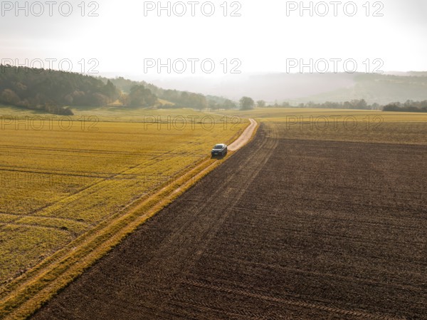 Landscape shot of a car on a path between golden and brown fields in sunlight, electric car VW ID5, Deer Carsharing, Gechingen, Black Forest, Germany, Europe