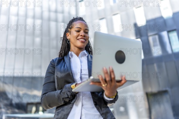 Portrait of a young successful latin businesswoman holding a laptop standing outside a financial building