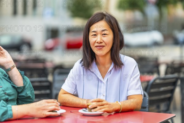 Asian woman drinking coffee with disabled friend in an outdoor cafeteria