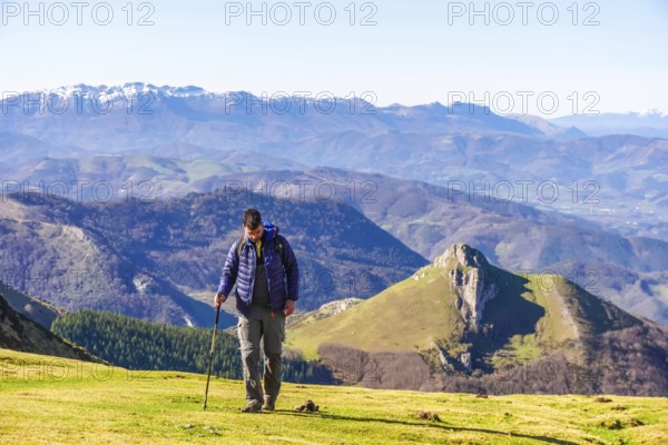 Male hiker walking on a grassy mountain slope with scenic views of the pyrenees mountains in the background