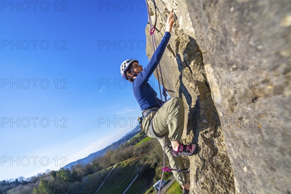 Female climber ascending challenging rock face on a sunny day, enjoying the thrill of outdoor adventure