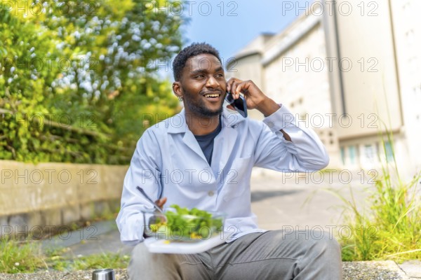 African doctor talking to the phone during lunch break sitting outside the hospital