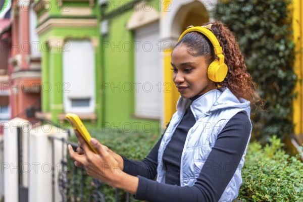 African american woman using phone while listening to music standing in a colorful street