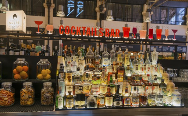 Eine gut bestückte Cocktailbar mit Flaschen verschiedener Spirituosen und bunter Beleuchtung in einer geschäftigen Umgebung, Mercado da Ribeira, Lissabon, Lisboa, Portugal, Europe