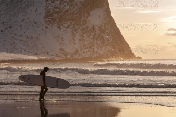 Surfer with surfboard under his arm on the beach of Unnstad, winter surfing, Lofoten Island Vestvågøya Lofoten, Northern Norway, Norway, Europe