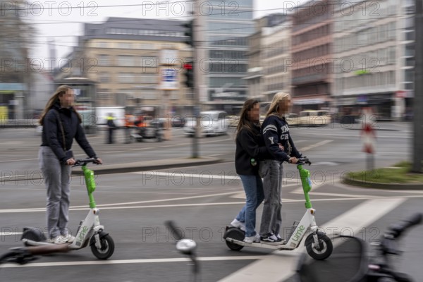 Young woman, two of them on an e-scooter, in the city centre, here at Neumarkt in Cologne, parked bikes and e-scooters at the roadside, bicycle lane, Cologne, North Rhine-Westphalia, Germany, Europe