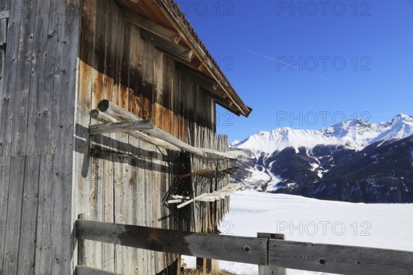 The Serfaus, Fiss, Ladis ski area in winter. In the foreground a wooden hut typical of the landscape, in the background a blue ski piste