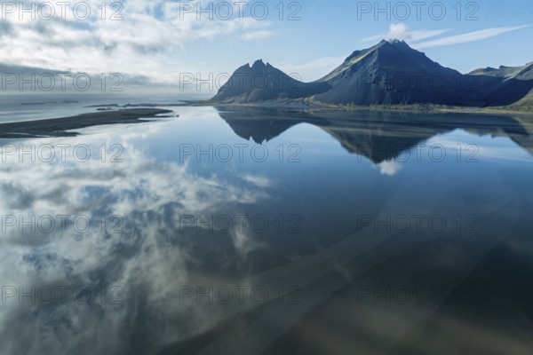 Aerial view over the calm sea to Mt. Brunnhorn and Vestrahorn, east of Höfn, clouds are reflected on the water, East Fjords, Iceland, Europe