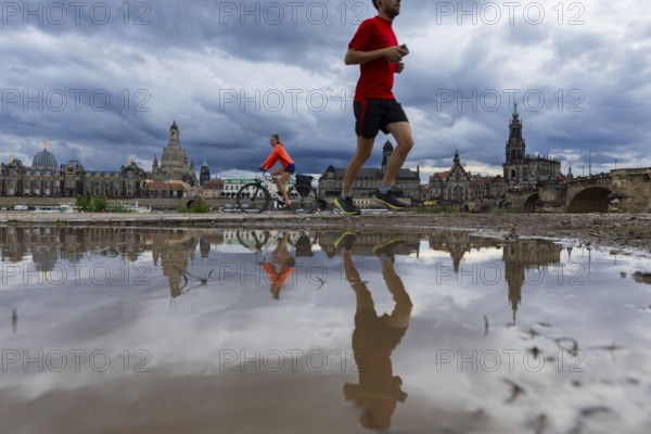 The silhouette of Dresden with a cyclist and a jogger and dark clouds behind the Church of Our Lady, reflected in a puddle on the Elbe cycle path, Elbe cycle path, Dresden, Saxony, Germany, Europe