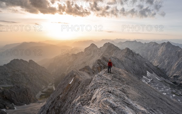 Mountaineer with helmet on a narrow rocky ridge at sunrise, crossing the Jubiläumsgrat, view of Höllental and Alpspitze, Wetterstein range, Bavaria, Germany, Europe