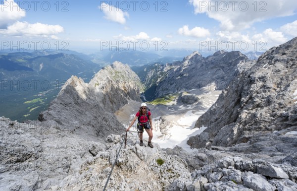 Mountaineer with helmet in a secured via ferrata, Zugspitze via ferrata, ascent to the Zugspitze, view of mountain basin with snow field of the Höllentalferner and Höllental, Wetterstein range, Wetterstein range, Bavaria, Germany, Europe